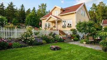 Kompakt robotgressklipper på en liten plen foran et lyst trehus